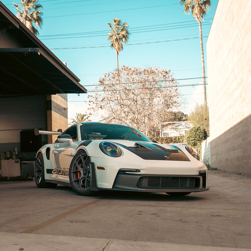 white porsche 911 gt3 rs in house automotive shop driveway with blue sky and palm trees in the background