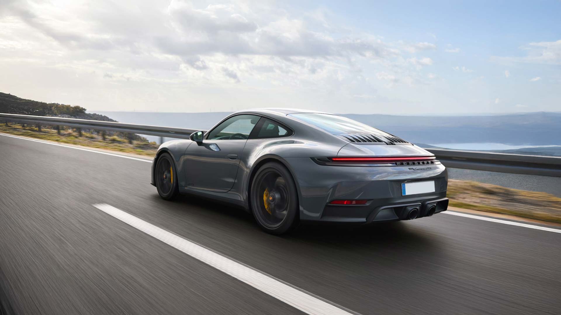 gray porsche 992 911 driving on scenic road by beach