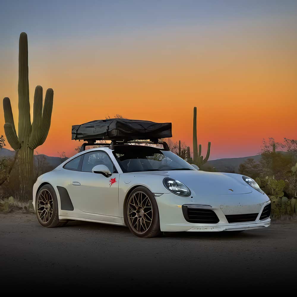 white porsche 911 in desert during sunset on dirt road with camper box on the roof