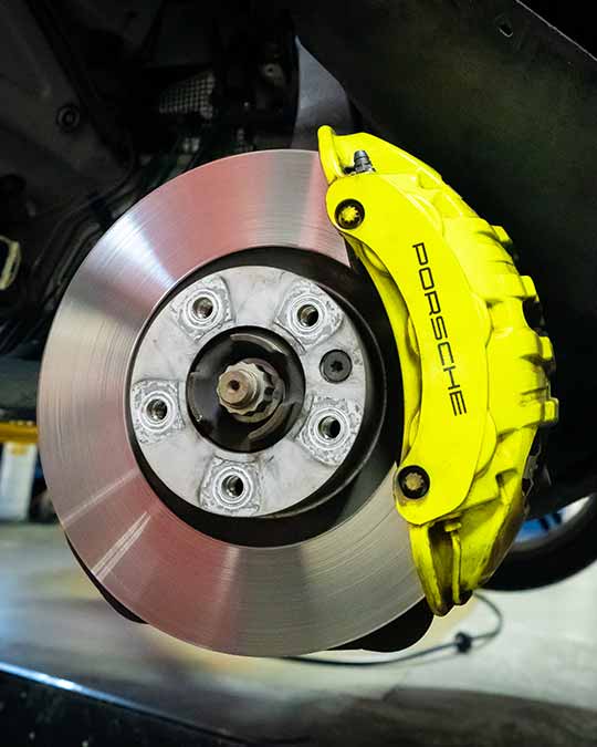 porsche service brake caliper and rotor maintenance showing yellow performance brakes