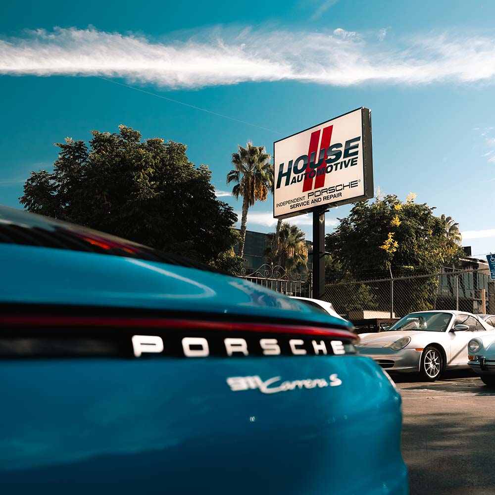 blue porsche 911 carrera a with the house automotive shop sign in focus in the background