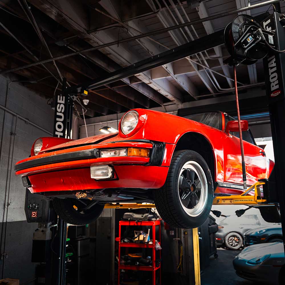 vintage red porsche 911 lifted on a car hoist in westlake porsche shop